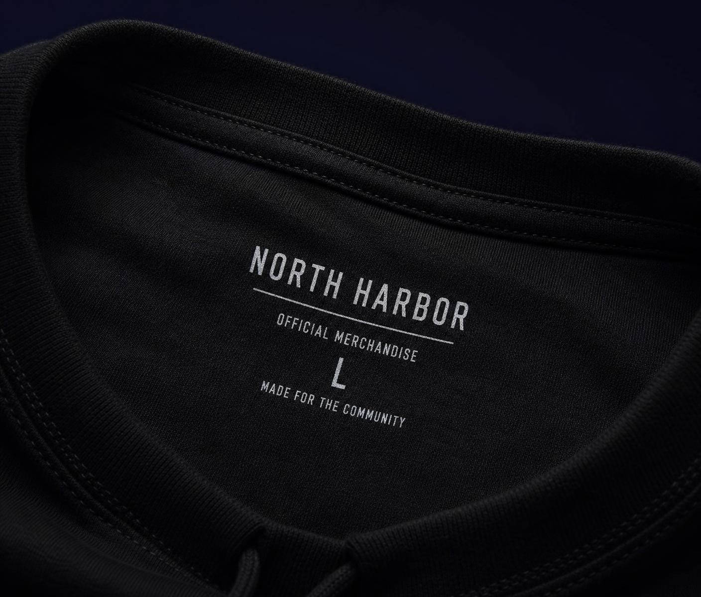 Close-up of a premium heavyweight garment inner neck with a custom printed white label reading NORTH HARBOR OFFICIAL MERCHANDISE L MADE FOR THE COMMUNITY